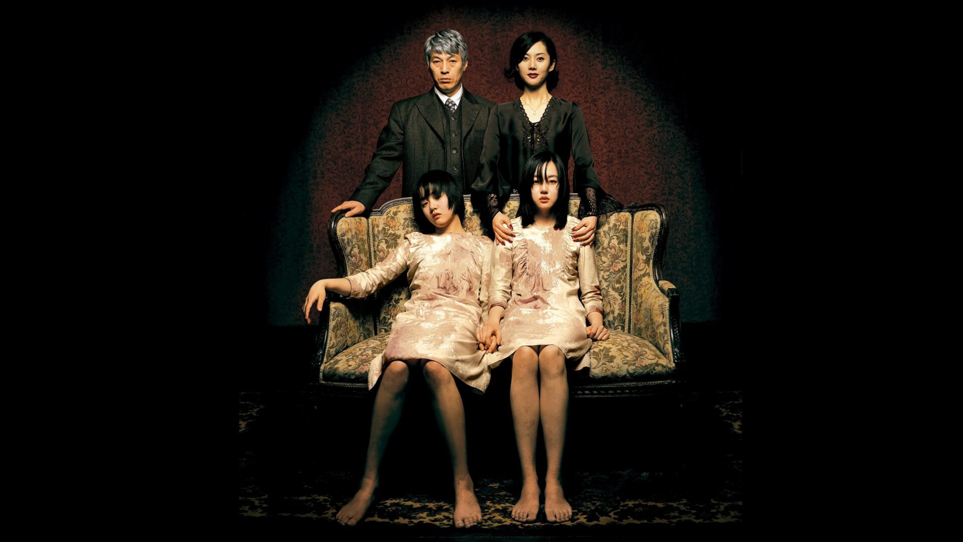 Zwei Kinder sitzen auf einem Sofa. Die Eltern stehen dahinter, alle schauen in die Kamera