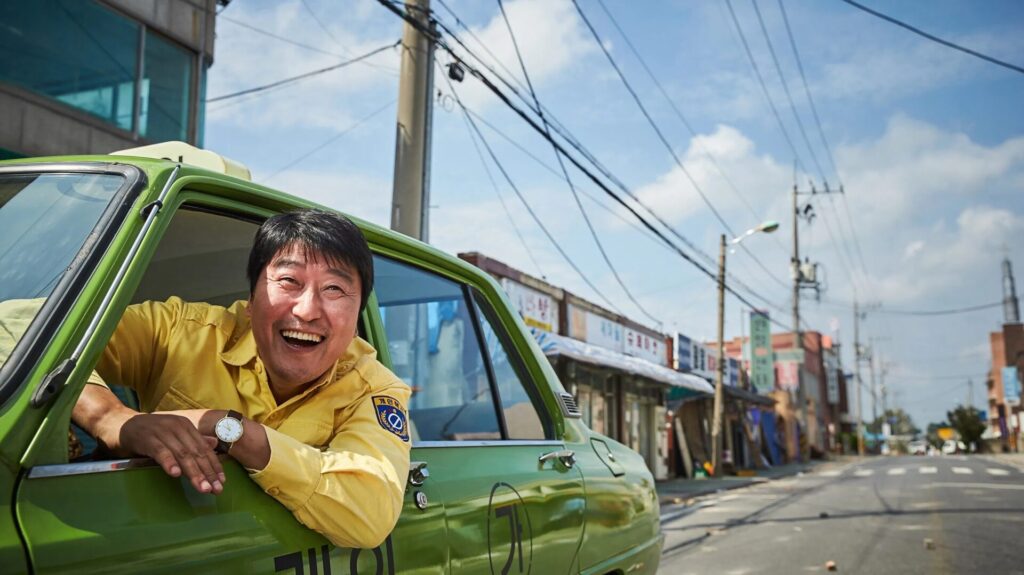 Song Kang-ho schaut lachend aus dem Taxi im Film "A Taxi Driver"