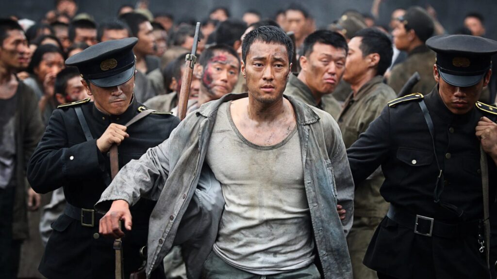 Die Hauptfigur aus "Battleship Island" wird von zwei japanischen Wachen vor einer Menschenmenge hergetrieben