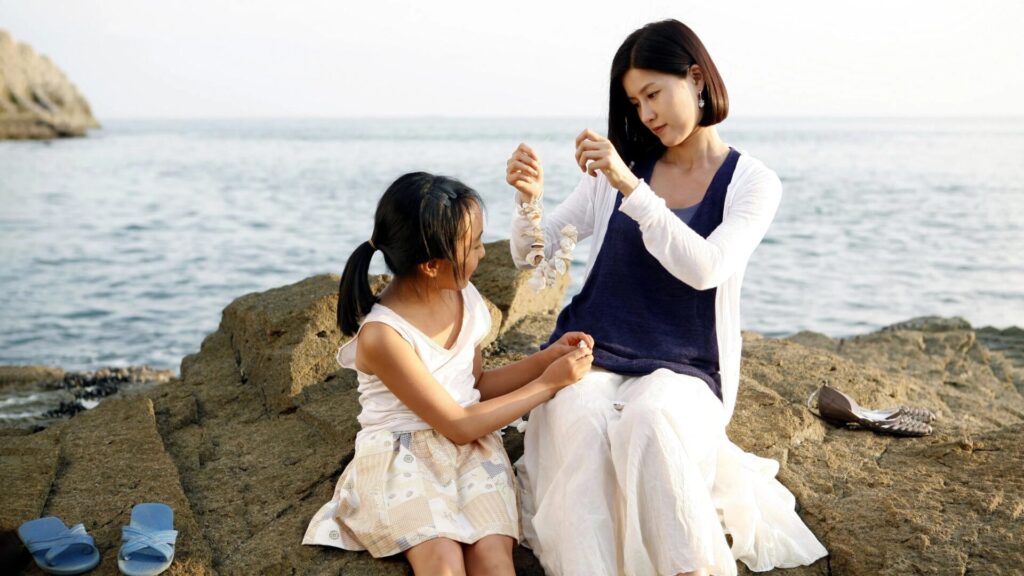 Eine Frau und ein Mädchen sitzen auf einem Felsen vor dem Meer und machen eine Muschelkette | Die 5 besten Filme aus Südkorea