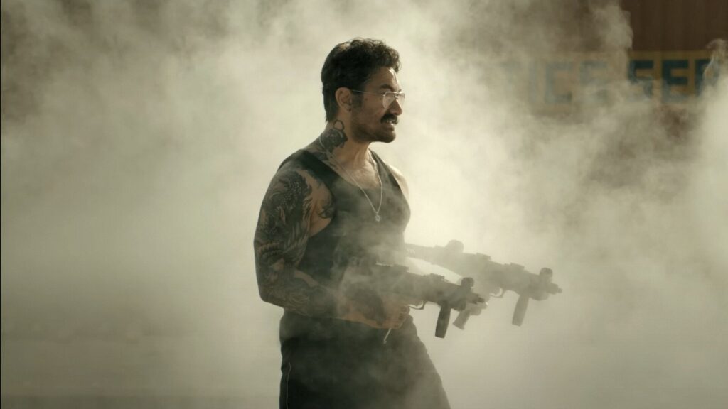 Das Bild zeigt Aamir Khan mit Maschinengewehren aus dem Film Coolie.