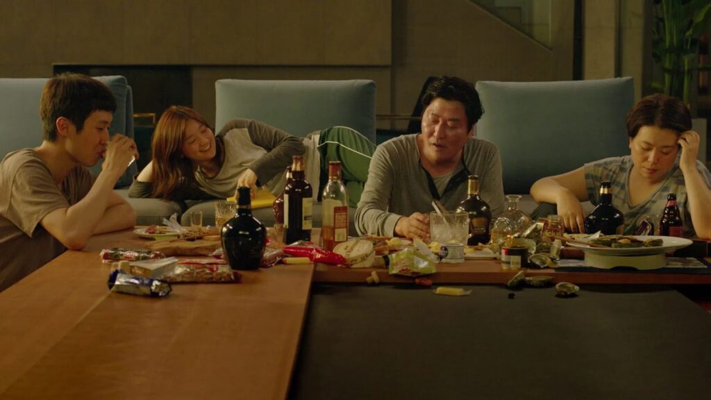 Die Familie Kim aus dem Film "Parasite" sitzt an einem Tisch mit diversen Flaschen und Speiseresten | Die 5 besten Filme aus Südkorea