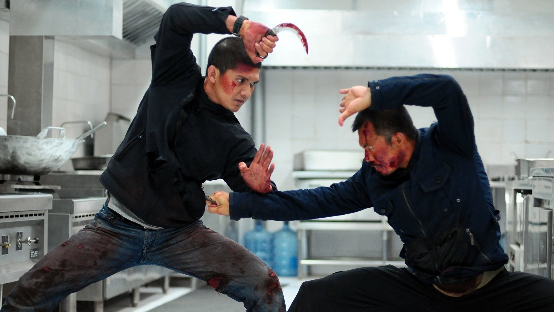 Zwei Männer kämpfen in einer Küche miteinander. Beide haben eine Stichwaffe in ihrer rechten Hand. Szene aus "The Raid 2".