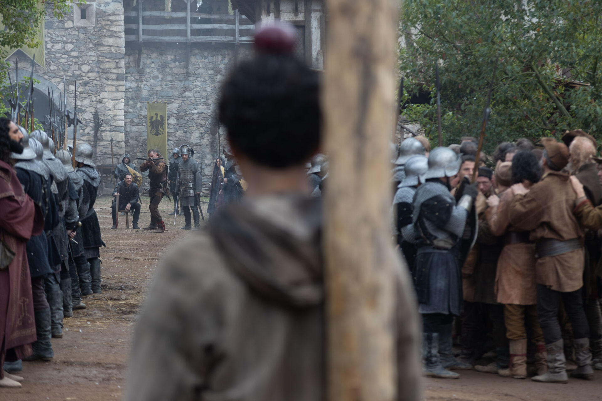 Der Apfelschuss: Wilhelm Tells Sohn mit dem Apfel auf dem Kopf von hinten. Links von ihm in der Ferne steht Tell mit der Armbrust und zielt.