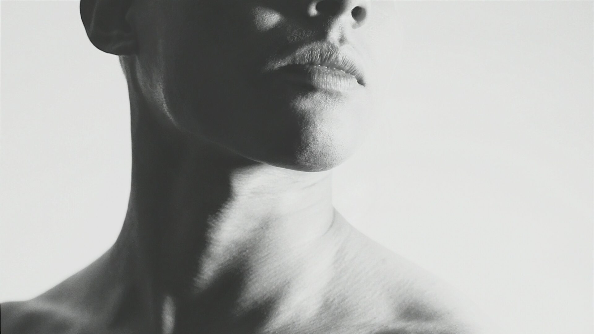 Schwarz-Weiß-Porträt eines Gesichts, teilweise angeschnitten, mit Fokus auf Lippen, Kinn und Hals.