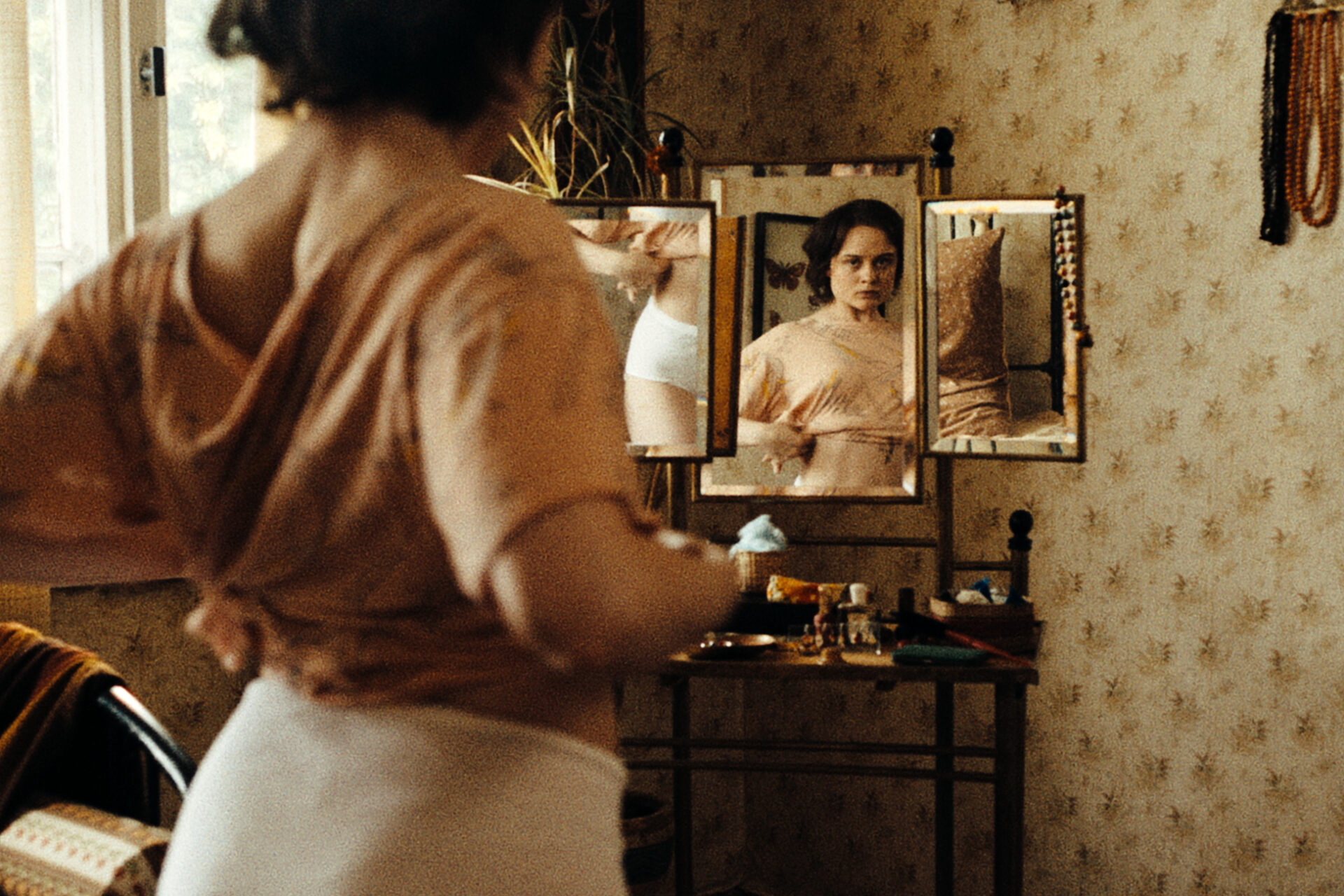 Das Bild zeigt eine Szene aus dem Film "In die Sonne schauen". Eine Frau probiert Kleidung an und schaut dabei in einen Spiegel.