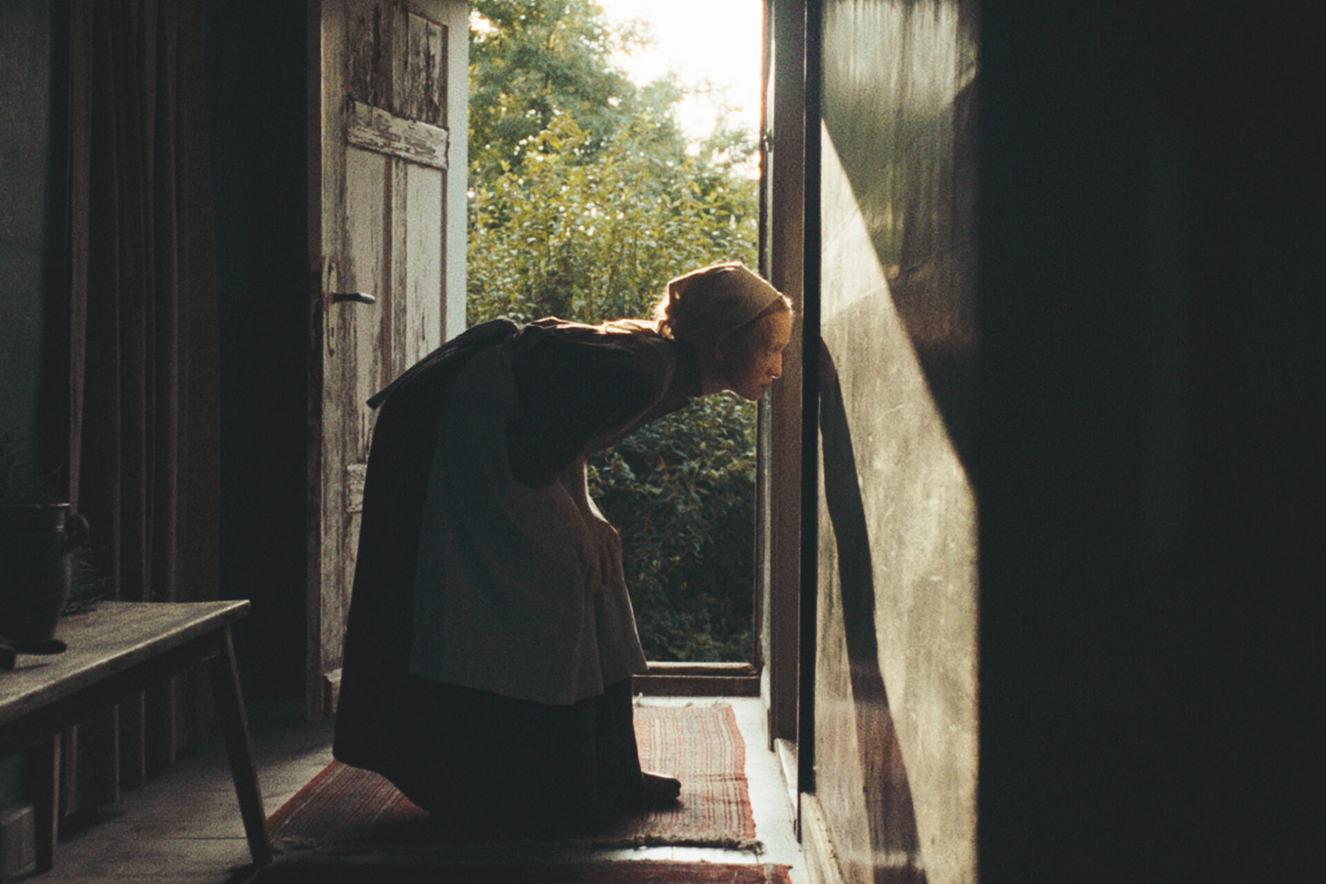 Das Bild zeigt eine Szene aus dem Film "In die Sonne schauen". Eine Person beugt sich vor und schaut durch ein Schlüsselloch.