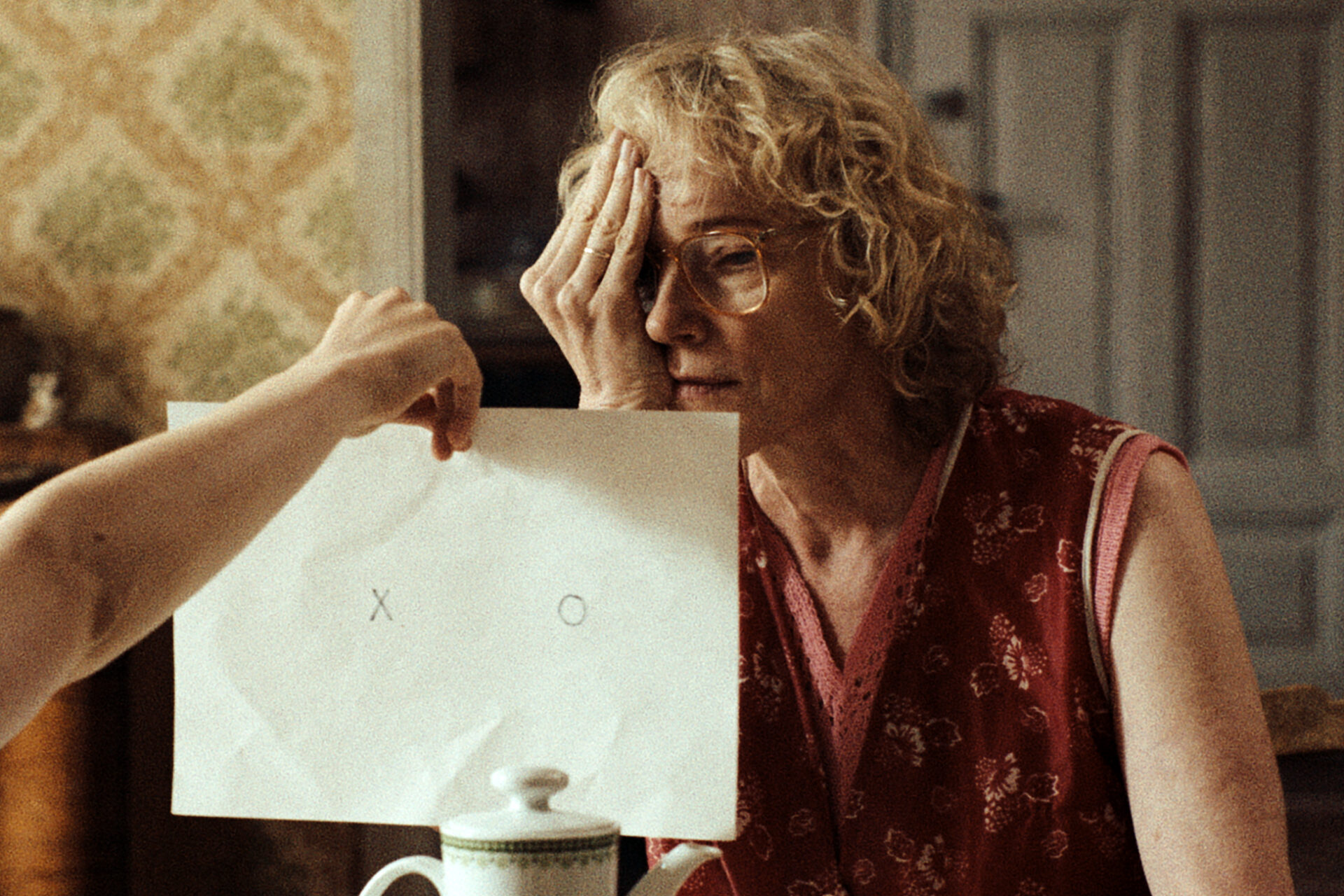 Das Bild zeigt eine Szene aus dem Film "In die Sonne schauen". Eine Frau hält sich ein Auge zu und blickt auf ein Stück Papier, dass ihr jemand anderes hinhält.