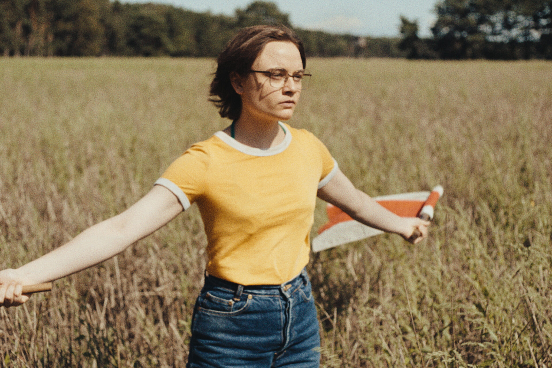 Das Bild zeigt eine Szene aus dem Film "In die Sonne schauen". Eine junge Frau steht mit einer Fahne in einem Weizenfeld.
