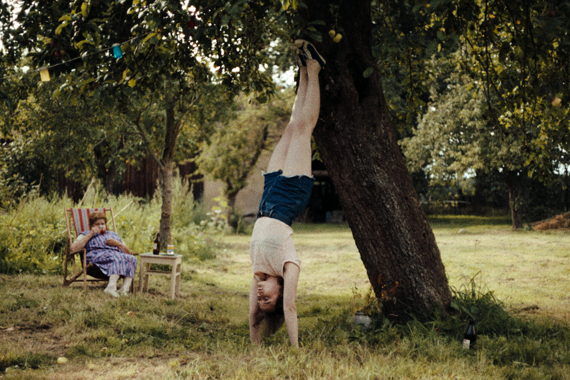 Das Bild zeigt eine Szene aus dem Film "In die Sonne schauen". Ein Mädchen macht einen Handstand an einen Baum gelehnt.