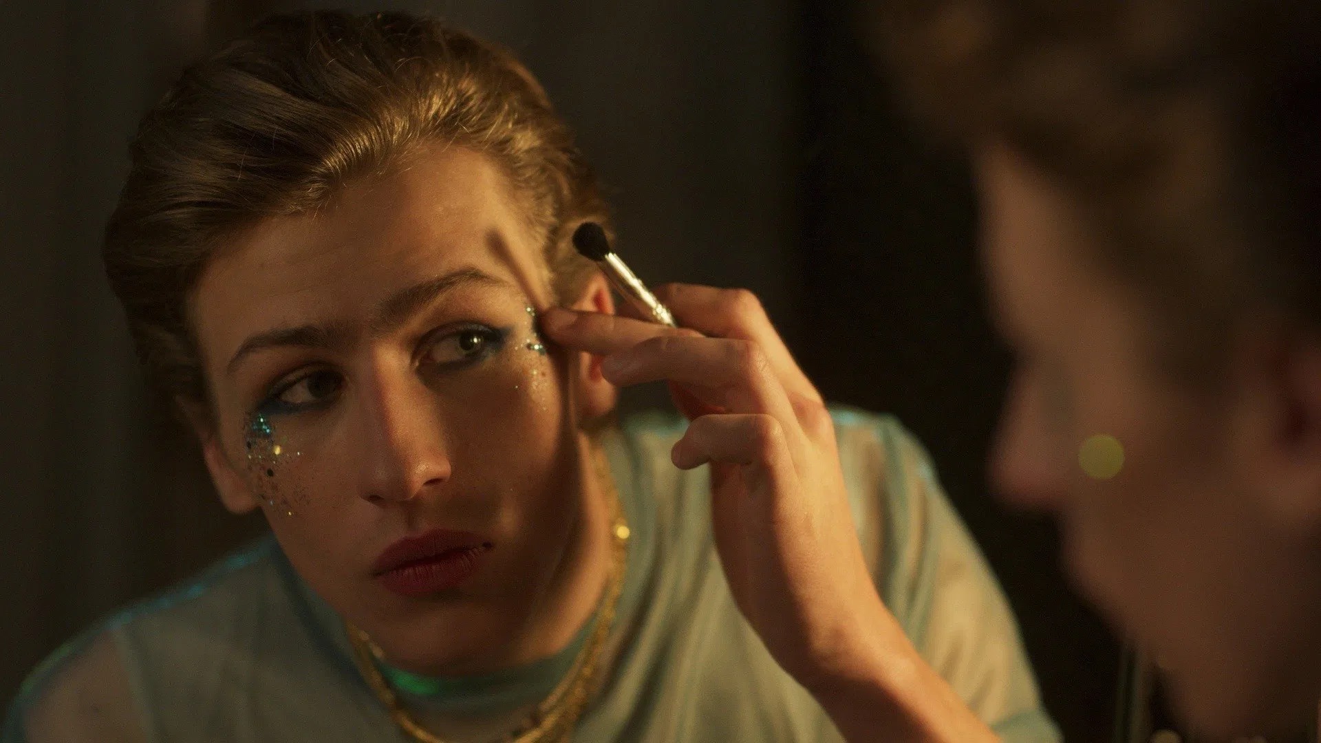 Das Bild zeigt Andrea (gespielt von Mattia Carrano) aus der Serie "Prisma", der sich gerade schminkt und sich Glitzer an die Augen klebt