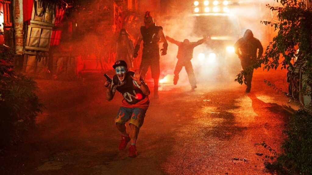 Eine Szene aus dem Film "The Toxic Avenger" eine Figur mit Clownsmake-up und Pistole im Vordergrund, im Hintergrund vier weitere Figuren, teilweise im Schatten