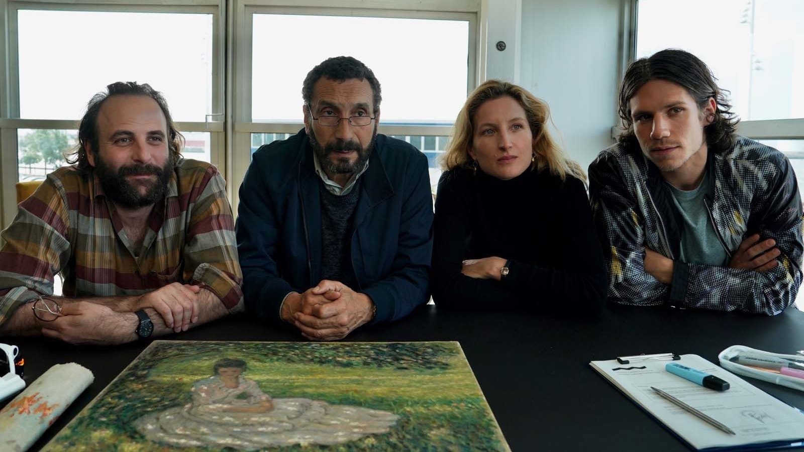 Vier Personen sitzen an einem Tisch. Auf dem Tisch ein buntes Gemälde. | Die Farben der Zeit