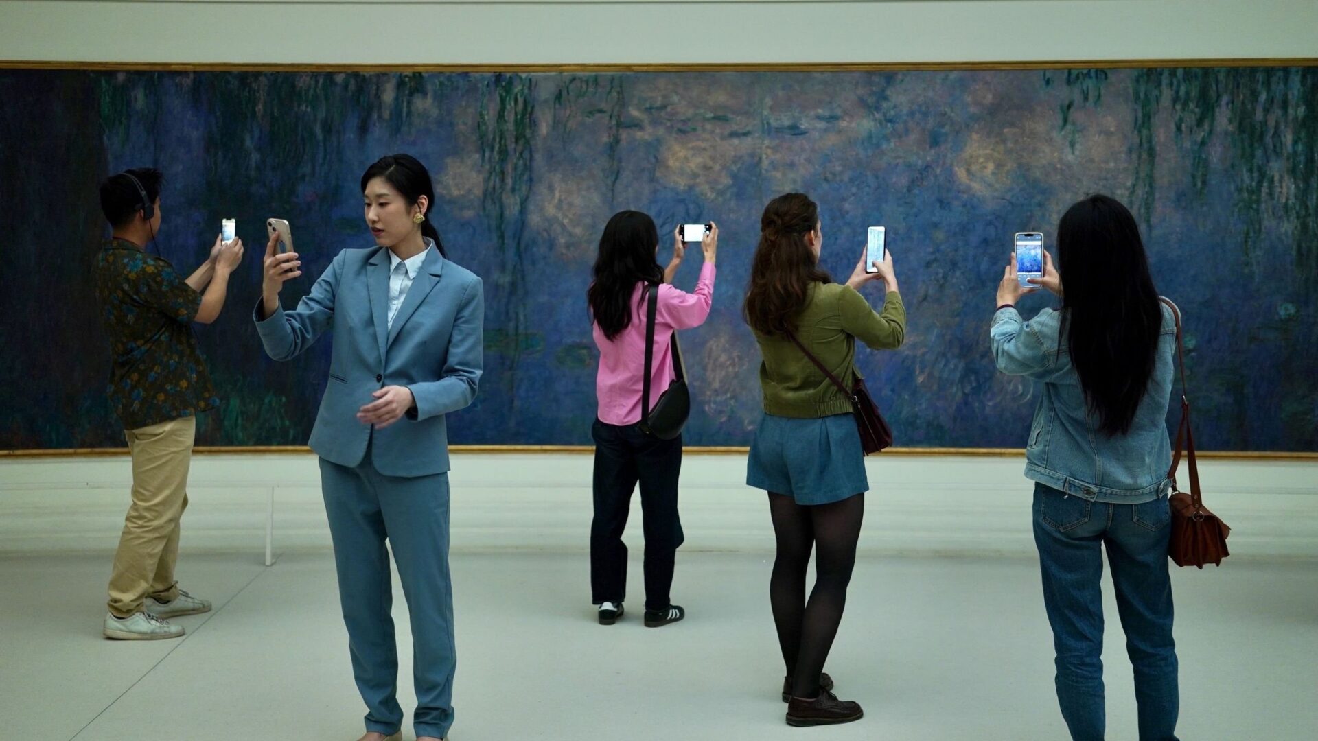 Mehrere Personen stehen vor einem Bild, schauen aber auf ihre Handys. | Die Farben der Zeit