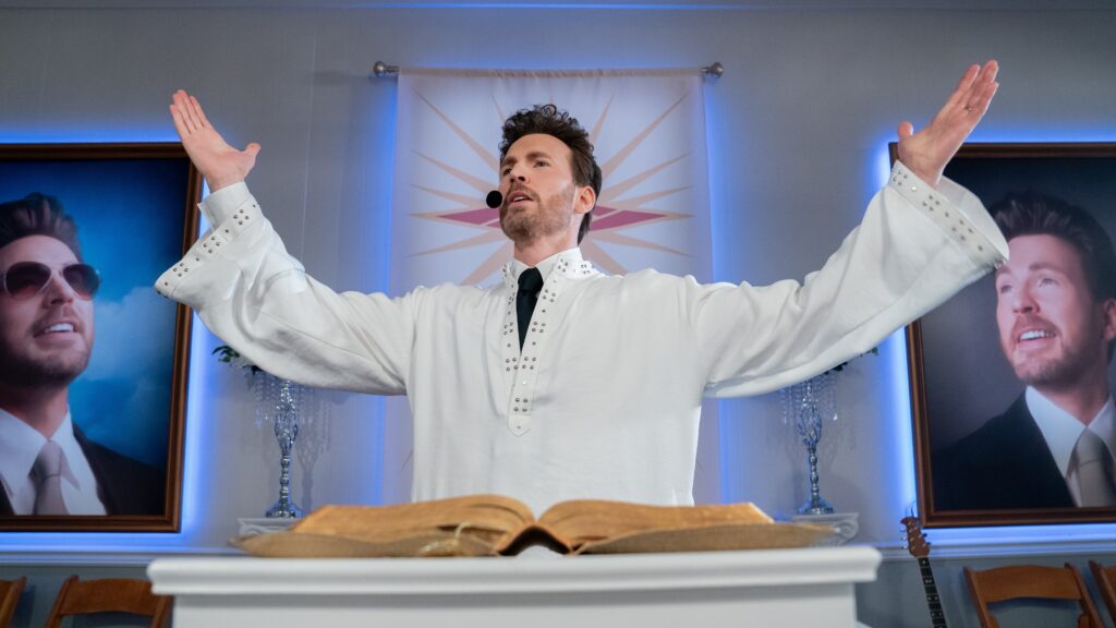 Reverend Drew Devlin (Chris Evans) predigt in einer Kirche. Im Hintergrund sind zwei Portraits von ihm zu sehen.