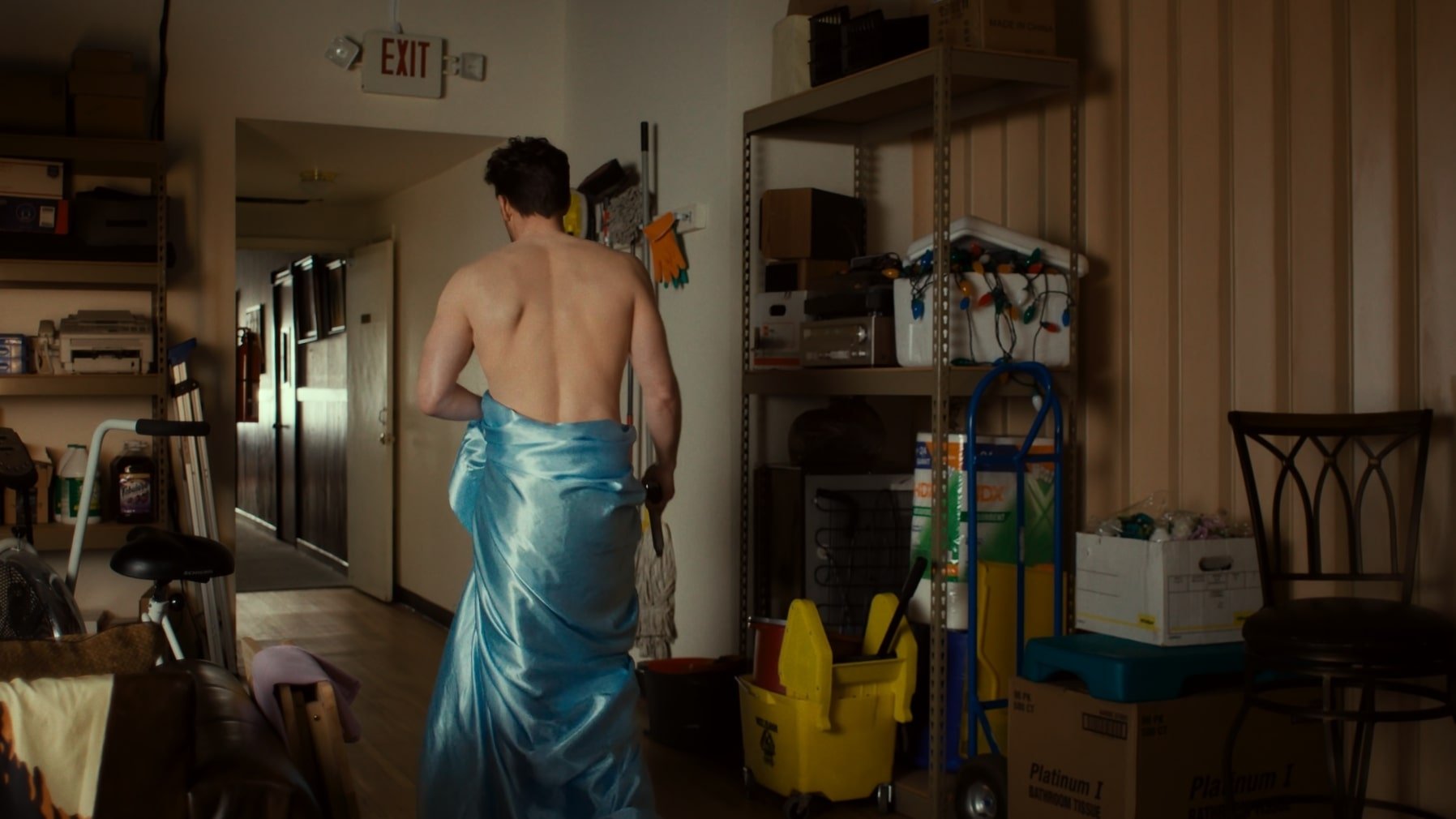 Ein nackter Mann mit einem Betttuch um die Hüfte hält eine Waffe.