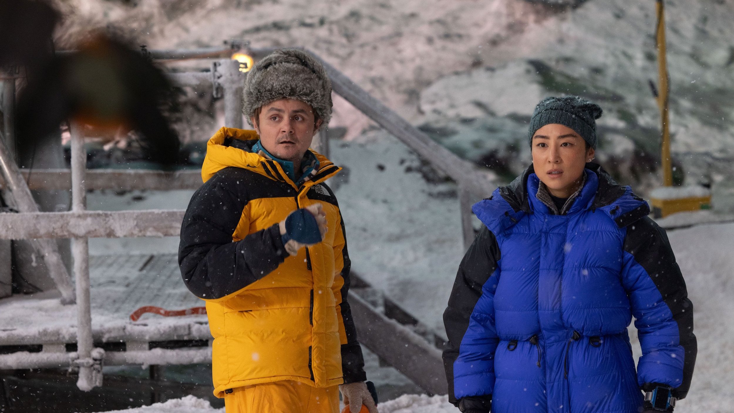 Eve Kim (Greta Lee) und ihr Kollege Seth Flores (Arturo Castro) stehen vor einem verschneiten Hintergrund.