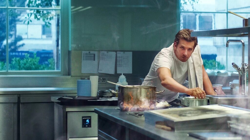 Bradley Cooper im Film "Im Rausch der Sterne" steht in einer Küche und bereitet seine Speißen vor. Er schaut dabei in die Kamera