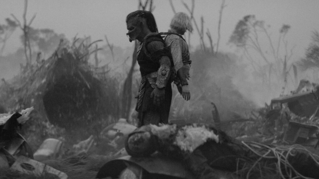 Dek hat den Oberkörper von Thea auf den Rücken gebunden, beide schauen auf eine zerstörte Umgebung | Predator: Badlands