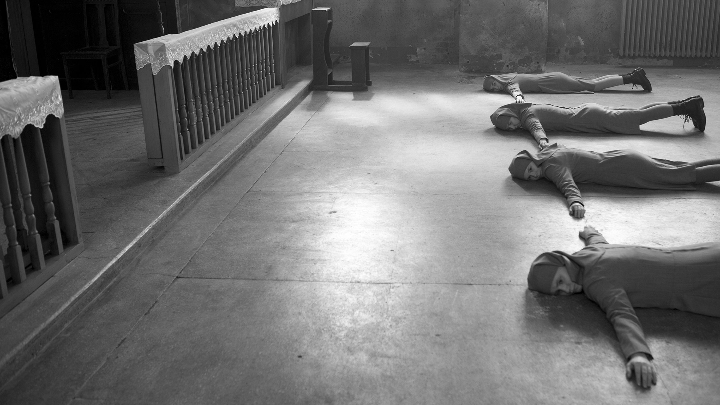 Drei Nonnen liegen mit ausgebreiteten Armen vor einem Altar.