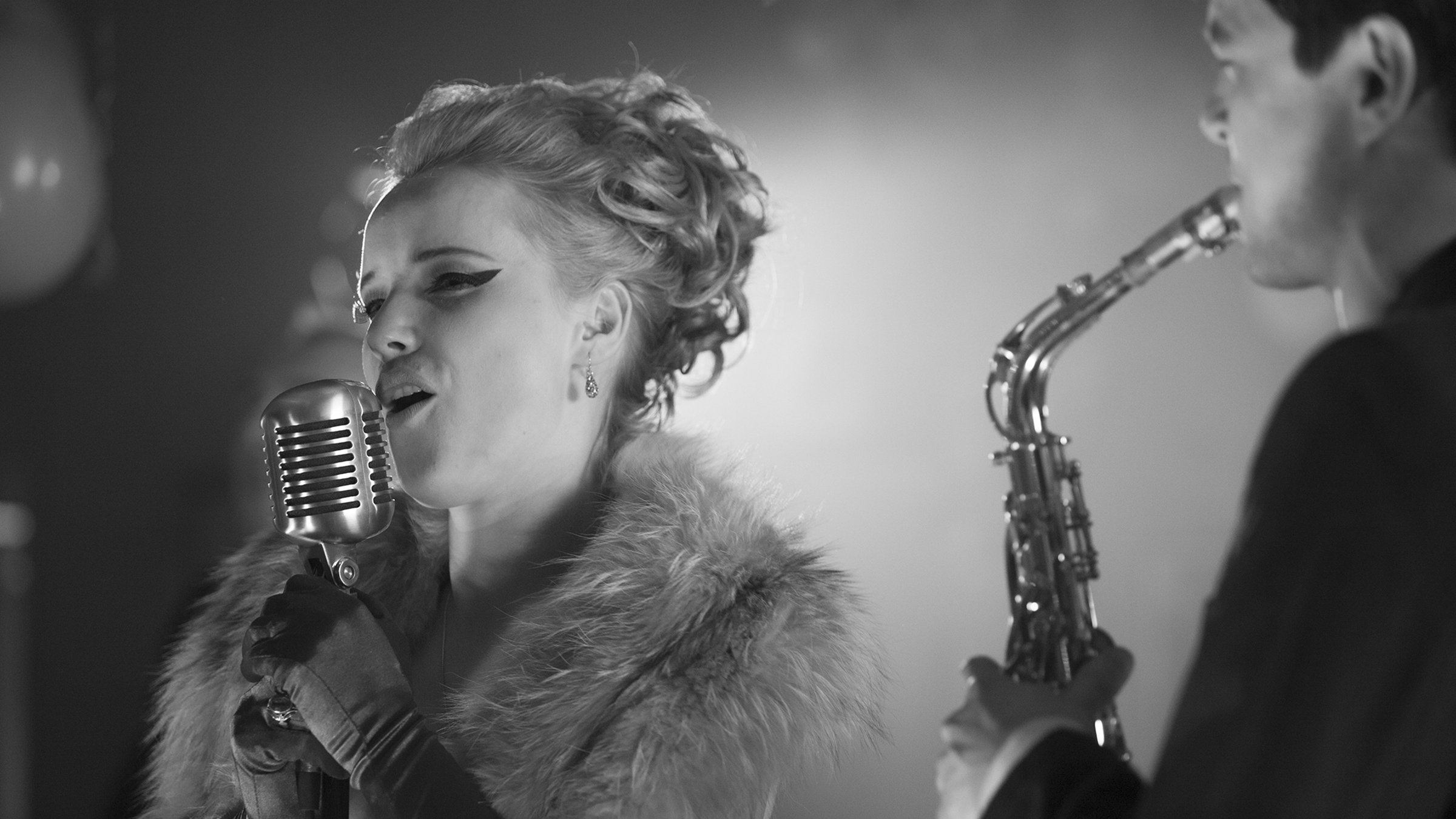 Eine Jazz-Sängerin (Joanna Kulig) und rechts daneben ein Saxofon-Spieler.