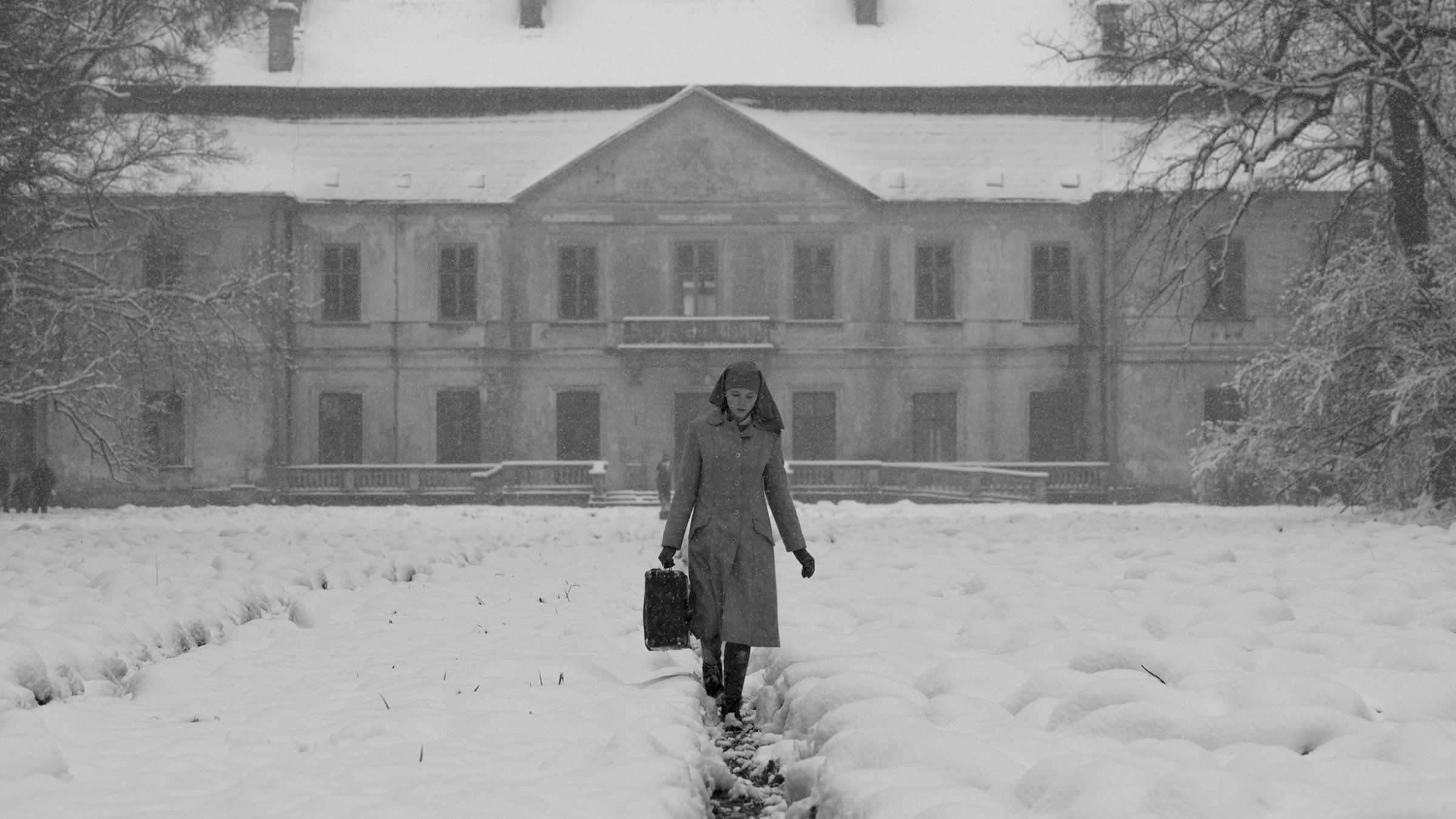 Anna entfernt sich von einem großen Herrenhaus mit einem Koffer. Links und rechts des Pfads liegt Schnee.