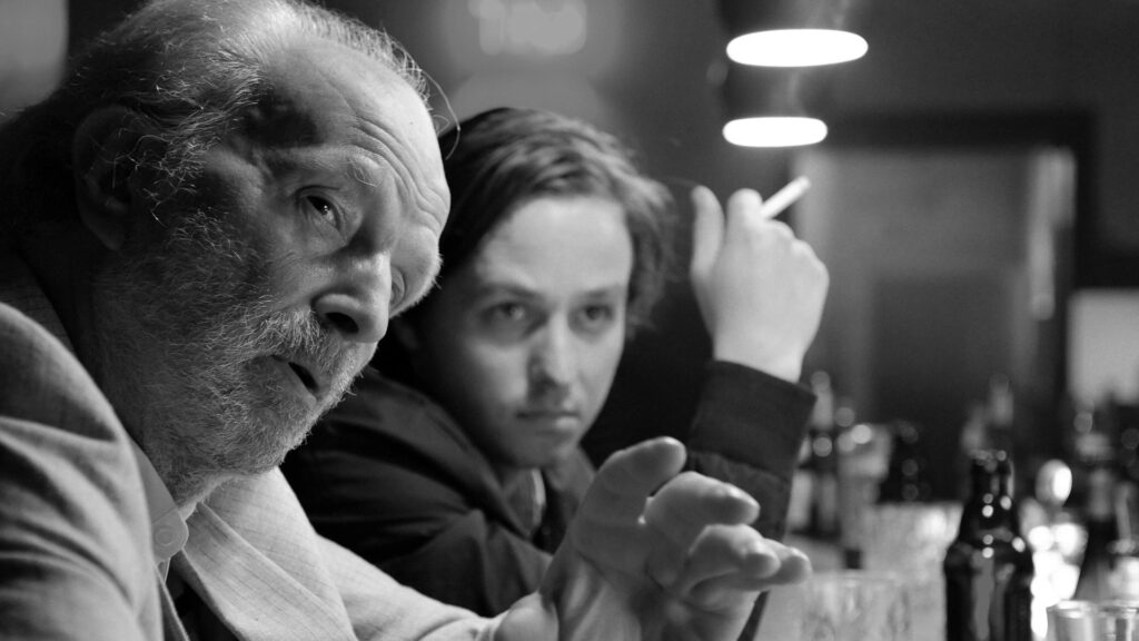 Michael Gwisdek und Tom Schilling sitzen rauchend und trinkend in einer Bar. | Monochrome Meisterwerke