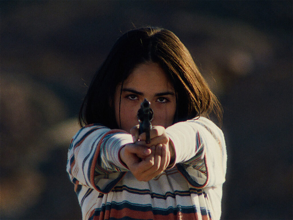 Das Bild zeigt Tamara Cortés mit einem Revolver in einer Szene des Films Der geheimnisvolle Blick des Flamingos