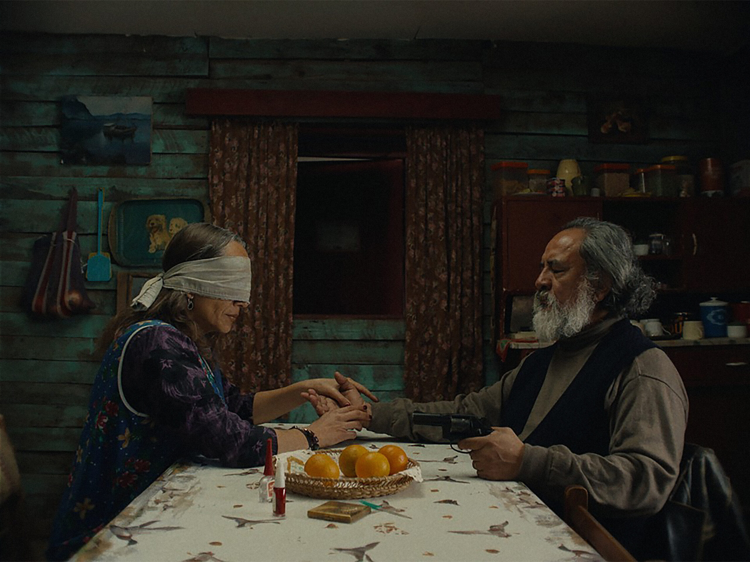 Das Bild zeigt zwei menschen, eine mit einer Augenbinde, an einem Tisch sitzend in einer Szene des Films Der geheimnisvolle Blick des Flamingos