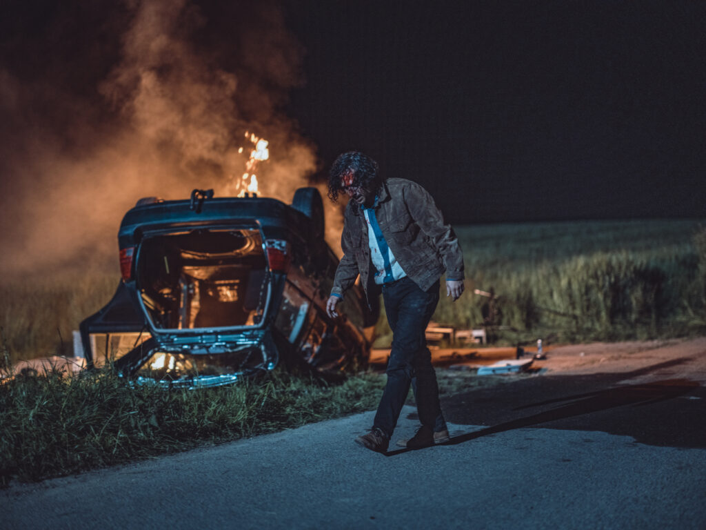 Das Bild zeigt Erkan Acar vor einem brennenden Auto in einer Szene des Films Make Me Feel