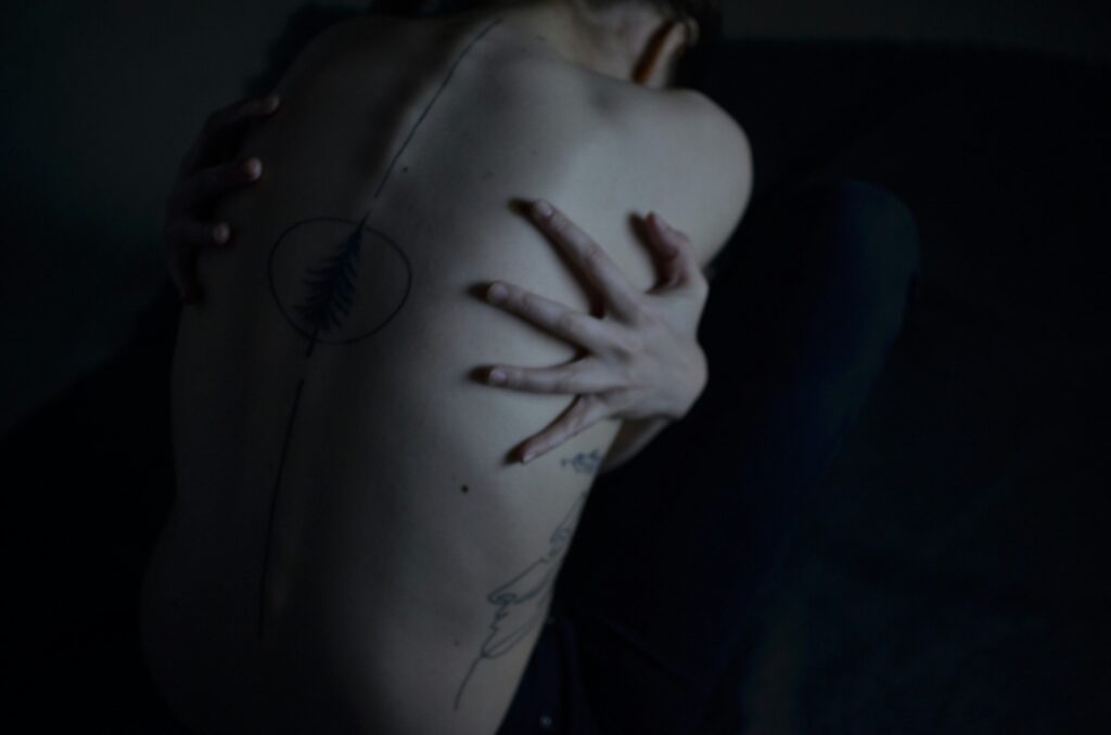 Das Bild zeigt eine Person mit nackten Oberkörper, Tattoos am RĂŒcken, die sich fest mit den HĂ€nden umschlingt | Media Monday #782