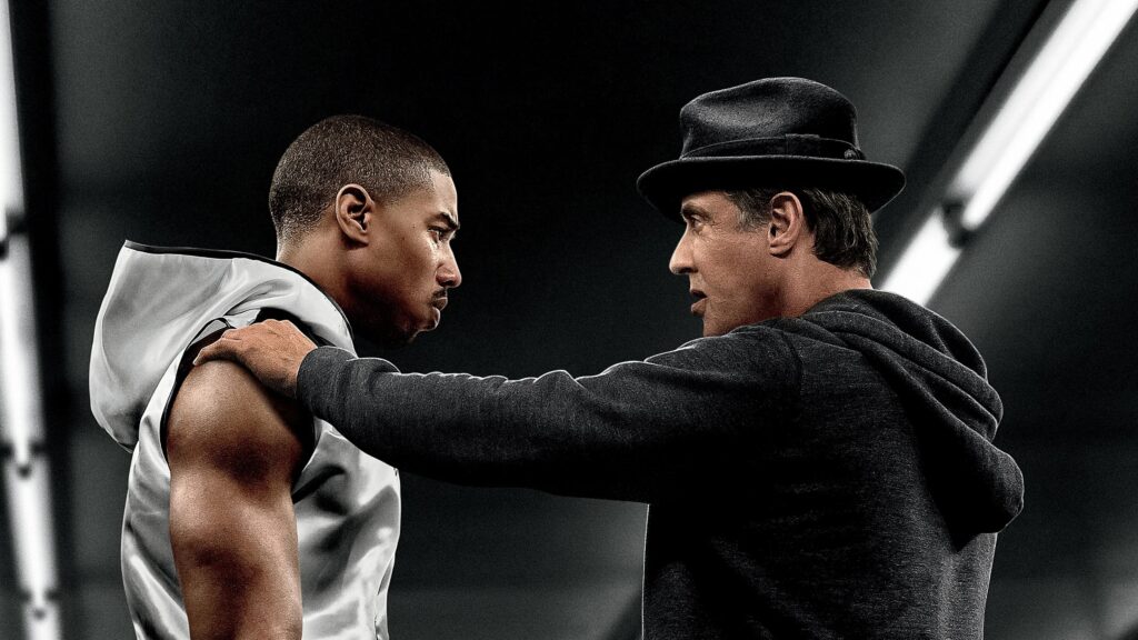 Adonis Creed (Michael B. Jordan) und Rocky (Sylvester Stallone) stehen sich gegenüber, Stallone hat seine Hand auf Jordans Schulter gelegt, eine Szene aus dem Film "Creed"  | Die 5 besten Box- und Kampfsportfilme