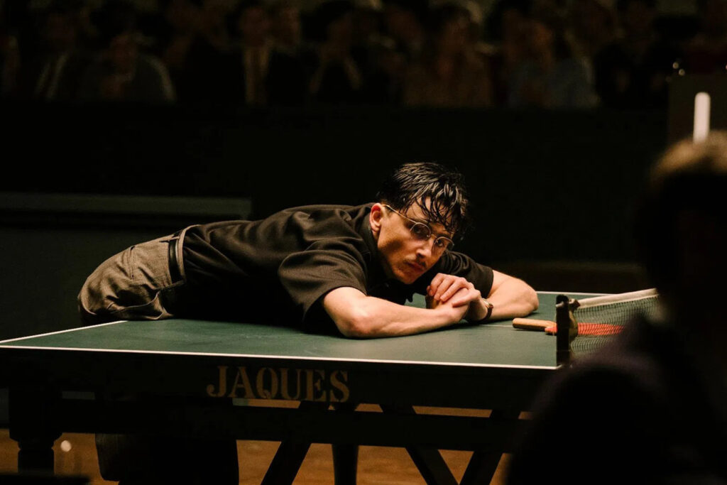 Das Bild zeigt Timothée Chalamet als Marty Mauser, der sich auf eine Tischtennisplatte stützt. Die Szene ist aus dem Film "Marty Supreme" | Media Monday #760