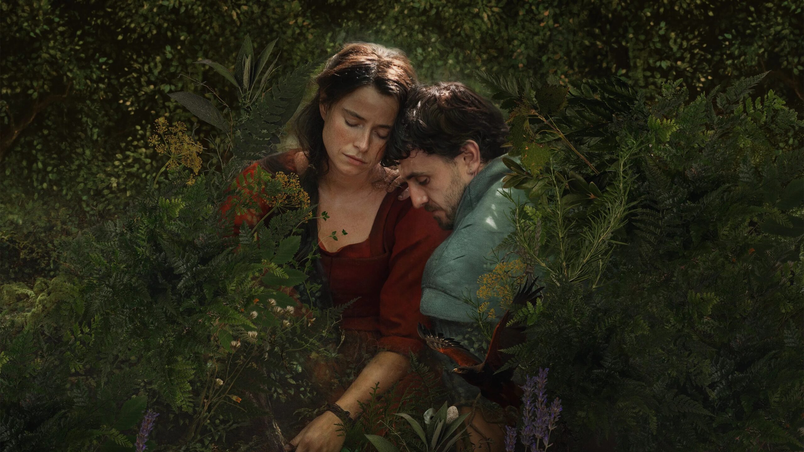 Das Bild zeigt Agnes (Jessie Buckley) und William Shakespeare (Paul Mescal) eng umschlungen, umgeben von Blumen und Grün. Die Szene ist aus dem Film Hamnet von Chloé Zhao