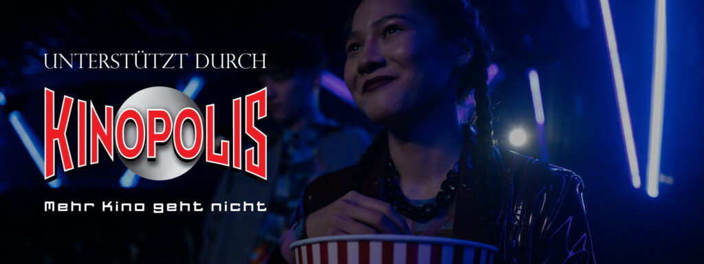 Eine Person sitzt im Kino und hält eine rot‑weiß gestreifte Popcorntüte in der Hand. Blaues Neonlicht beleuchtet die Szene. Links im Bild steht der Schriftzug „Unterstützt durch Kinopolis – Mehr Kino geht nicht“ neben dem Kinopolis‑Logo.