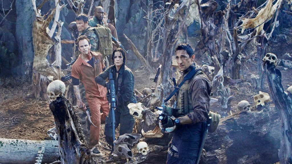 Eine Gruppe von Menschen stehen in einer mit Knochen und Ästen dekorierten Landschaft, im Vordergrund steht Adrien Brody, eine Szene aus dem Film "Predators"