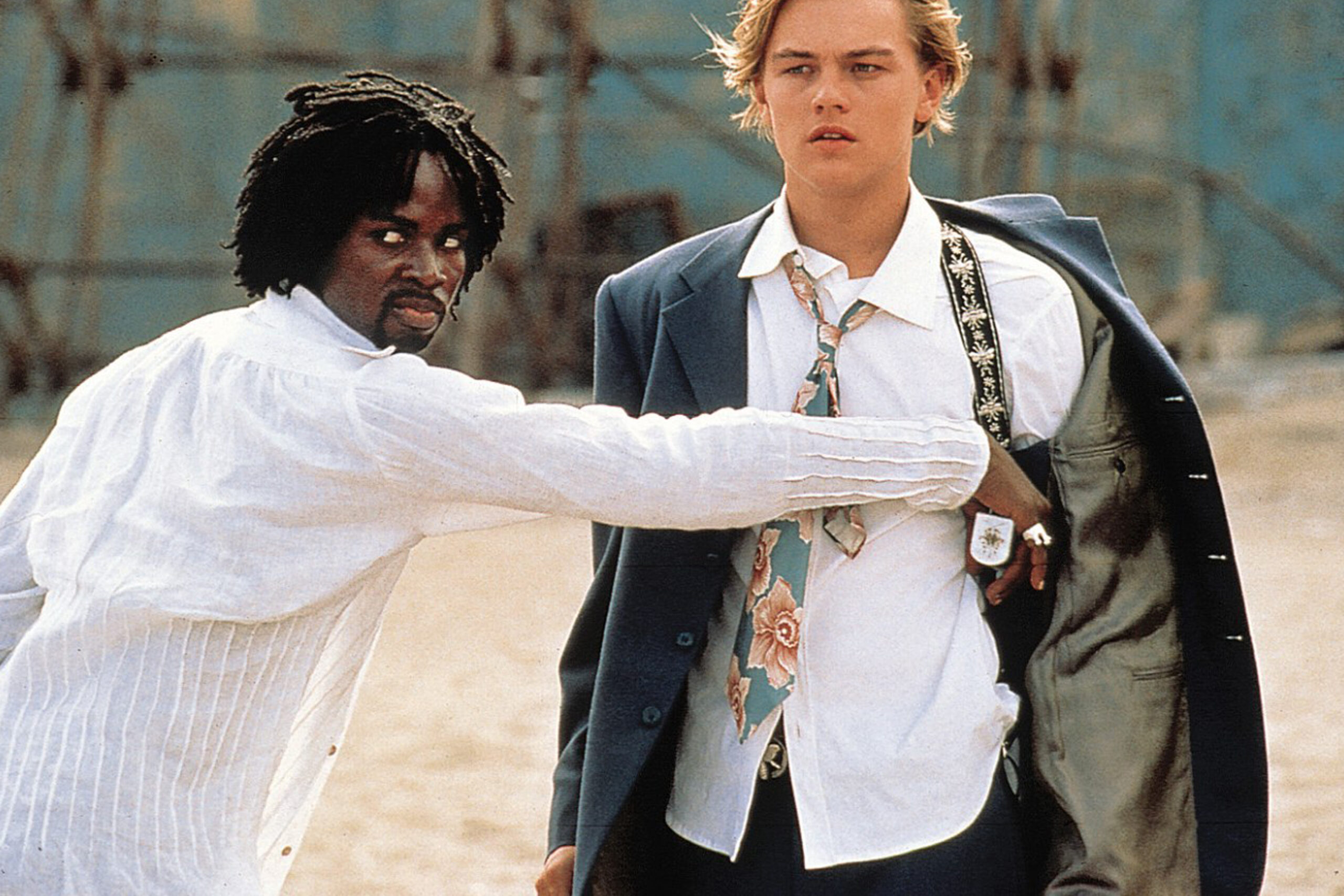 Das Bild zeigt Mercutio (Harold Perrineau) und Romeo (Leonardo DiCaprio) am Strand von Mexiko. Mercutio zieht gerade die Waffe von Romeo aus dessen Halfter