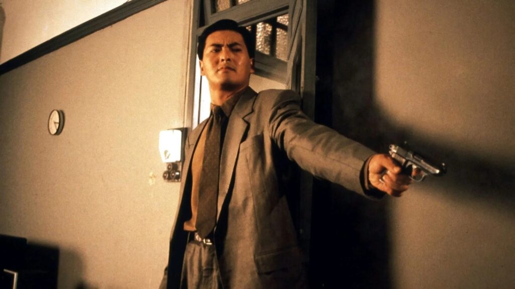 Chow Yun-Fat steht vor einer Tür und streckt eine Pistole von sich weg | Die 5 besten asiatischen Actionstars