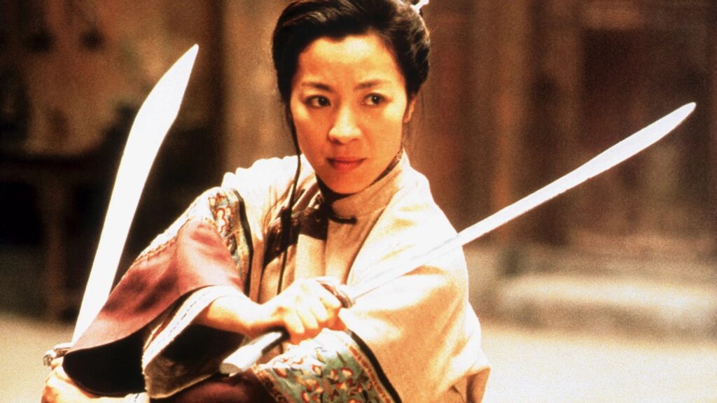 Michelle Yeoh hält zwei Schwerter und schaut kampfbereit in die Kamera | Die 5 besten asiatischen Actionstars