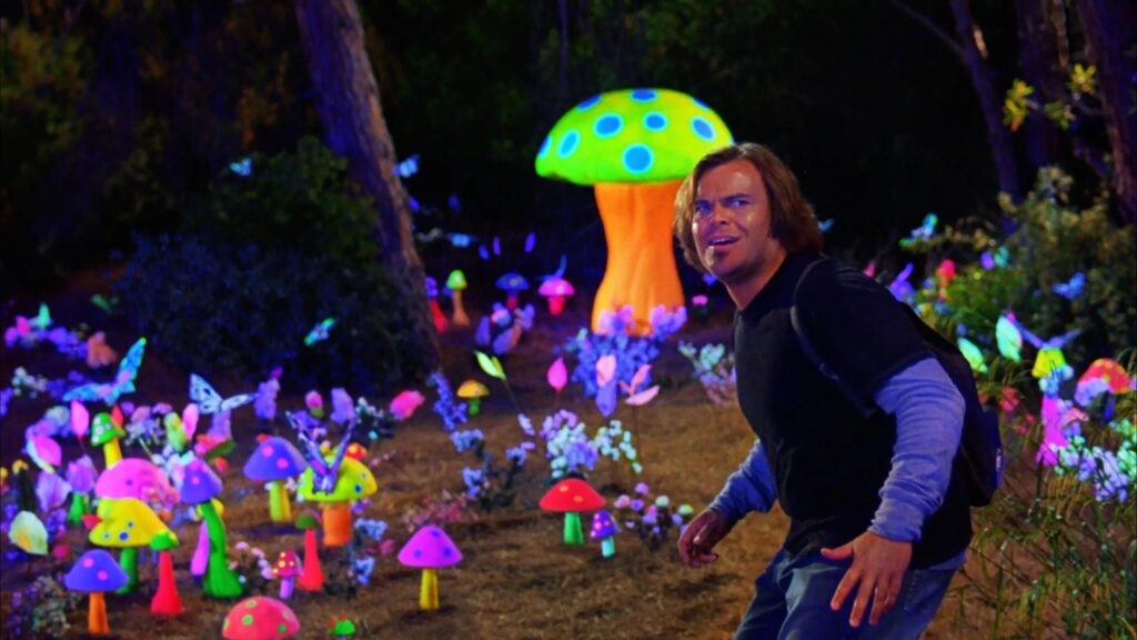 Jack Black schleicht durch einen Wald, dahinter sind viele bunte und leuchtende Pilze