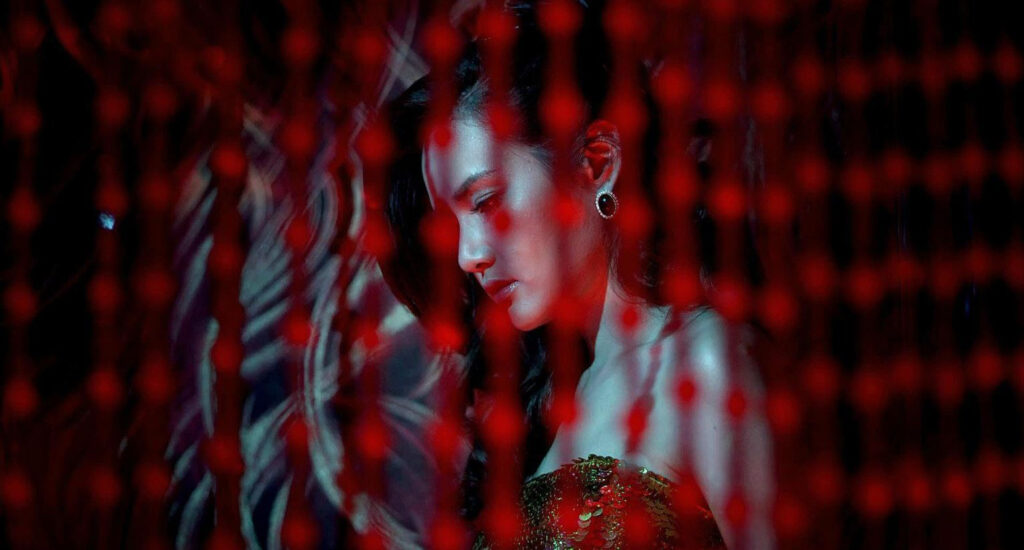 Vithaya Pansringarm in Only God Forgives, im Profil vor dramatischer Beleuchtung aus roten und blauen Neonfarben. Im Vordergrund leuchten unscharfe rote Lichtpunkte. Die Szene wirkt intensiv, stilisiert und typisch für die visuelle Ästhetik des Films. | Themenübersicht April 2026