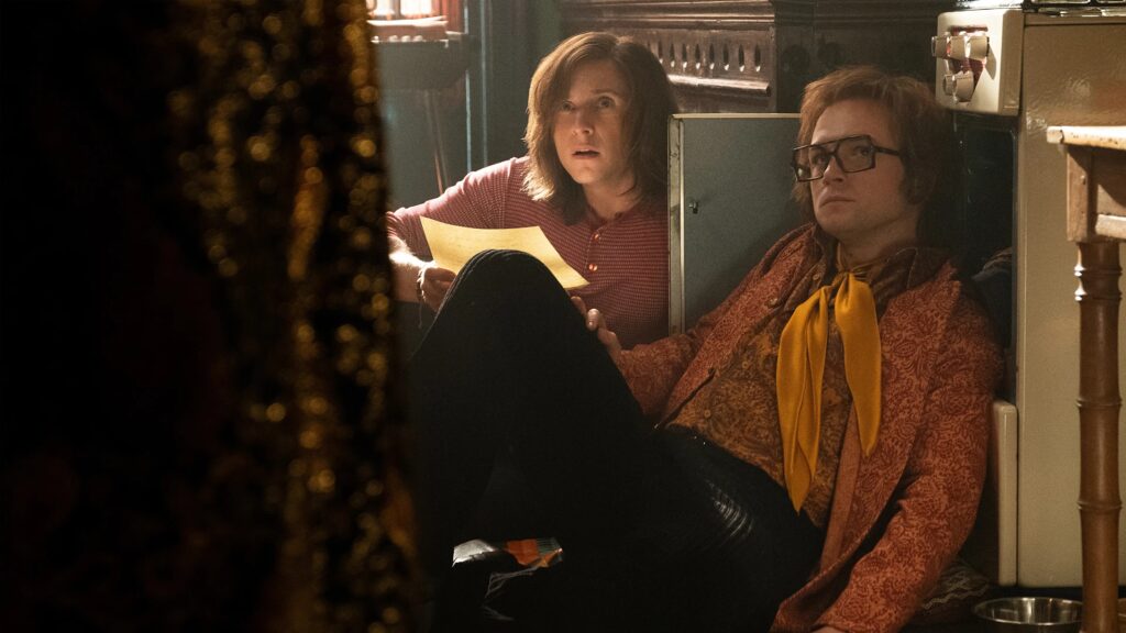 Elton John und Bernie Taupin sitzen am Boden vor Schränken und schauen erschrocken nach vorne | Die 5 besten Musik-Biopics
