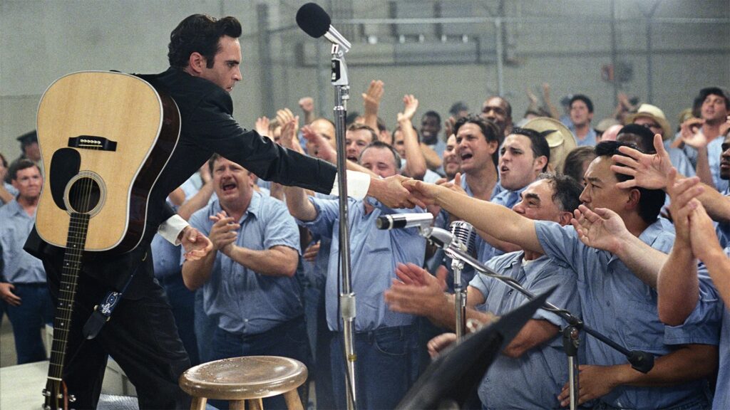 Joaquin Phoenix als Johnny Cash steht auf einer Bühne, während vor ihm eine Gruppe Häftlinge steht, die ihm die Hand geben wollen | Die 5 besten Musik-Biopics