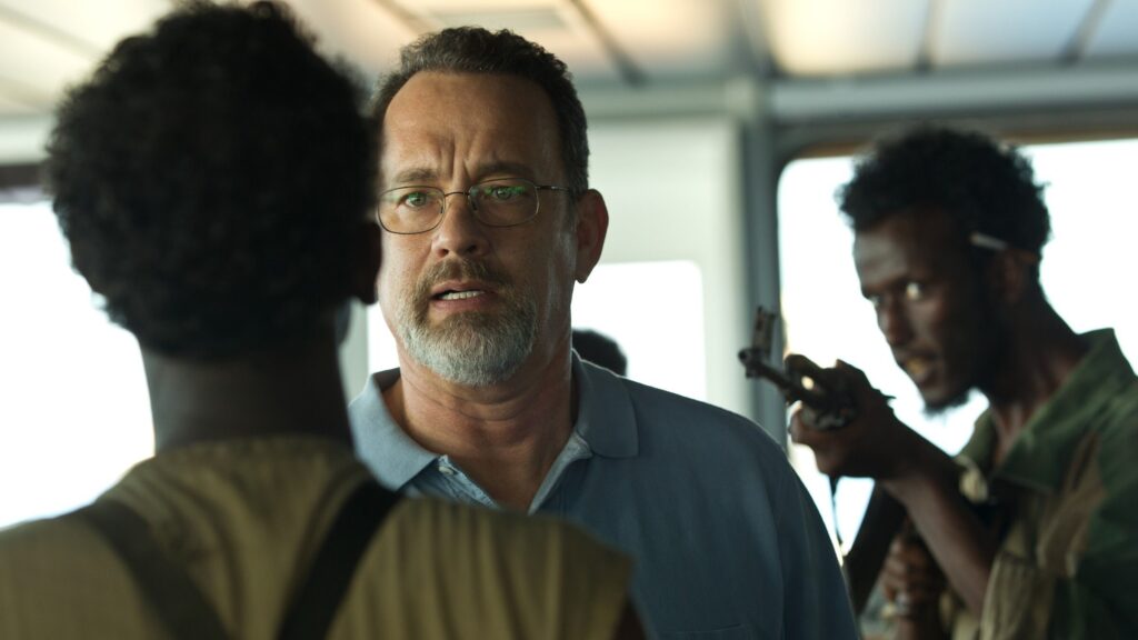 Captain Phillips und zwei Piraten. Einer steht hinter ihm und zielt mit einem Gewehr auf ihn. | Die 5 besten Filme mit Piraten