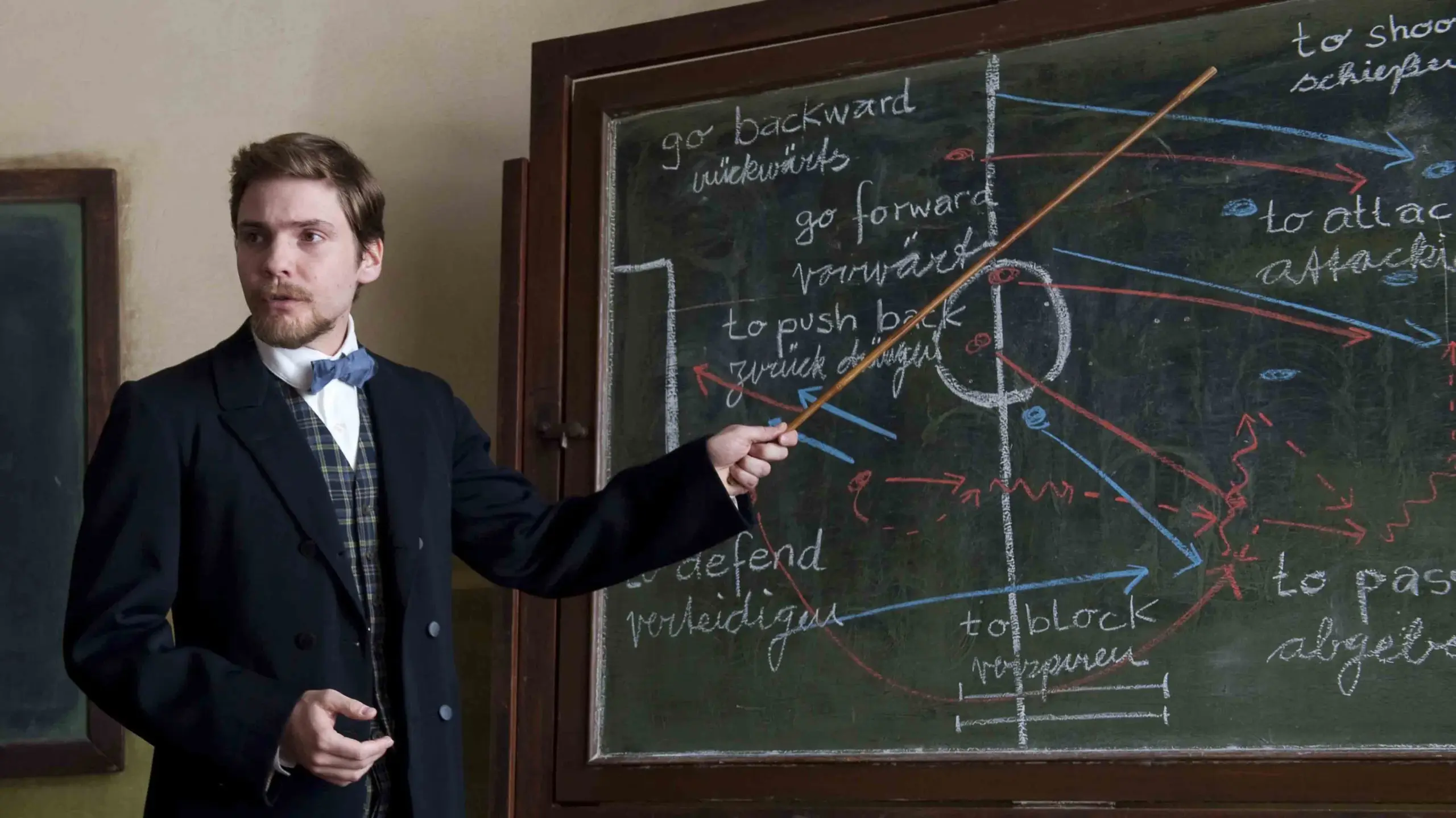 Das Bild zeigt Daniel Brühl als Lehrer Konrad Koch beim erklären von Fußball regeln an einer Tafel.