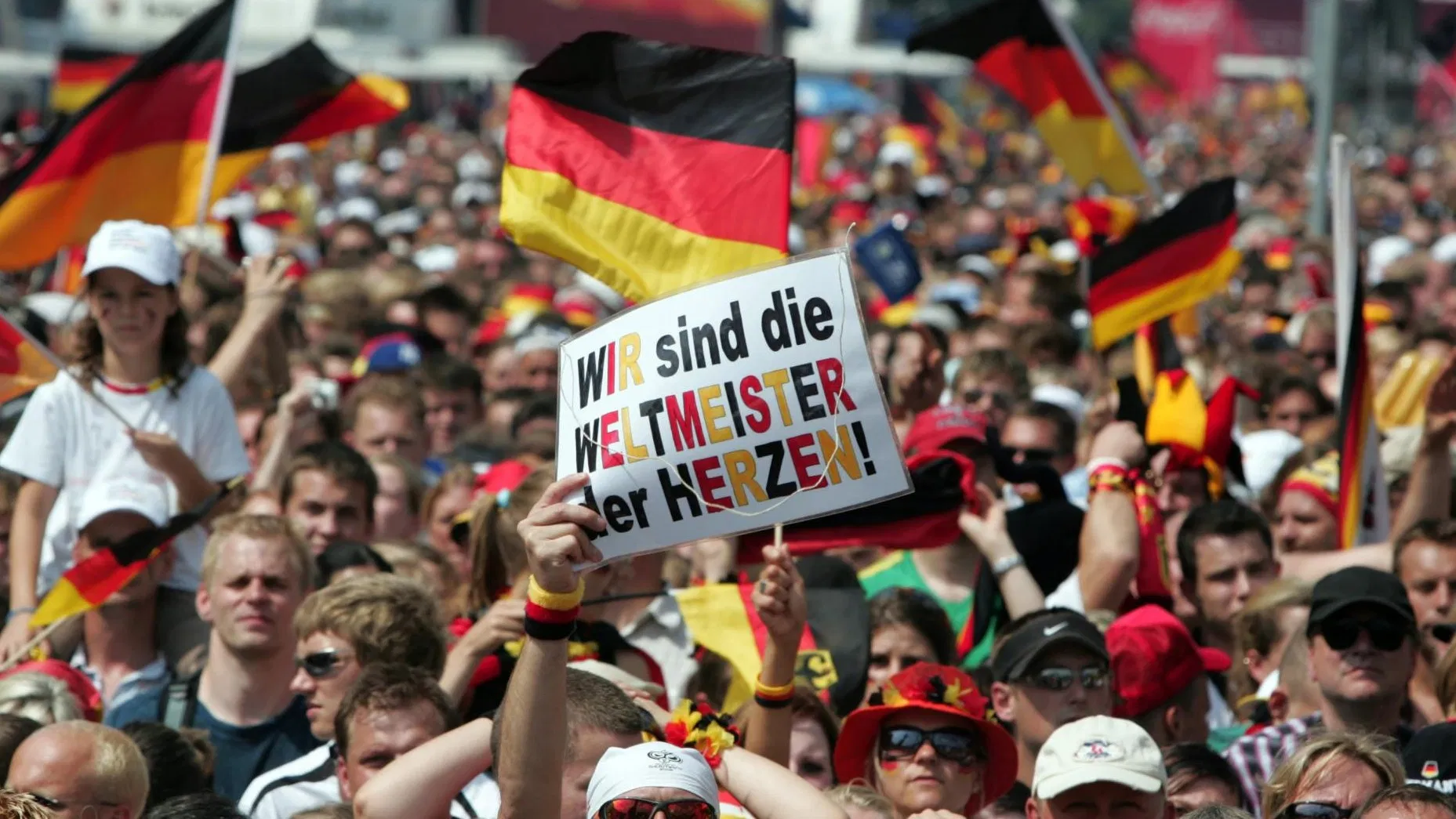 Das Bild zeigt eine Menge Menschen mit Deutschlandfahnen und einem hochgehaltenen Schild auf dem Deutschland Weltmeister der Herzen steht