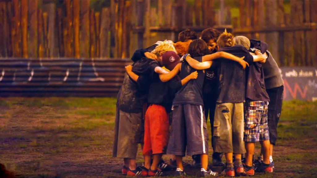 Das Bild zeigt eine Gruppe Kinder, die in einem Kreisformiert auf einem Fußballfeld stehen.