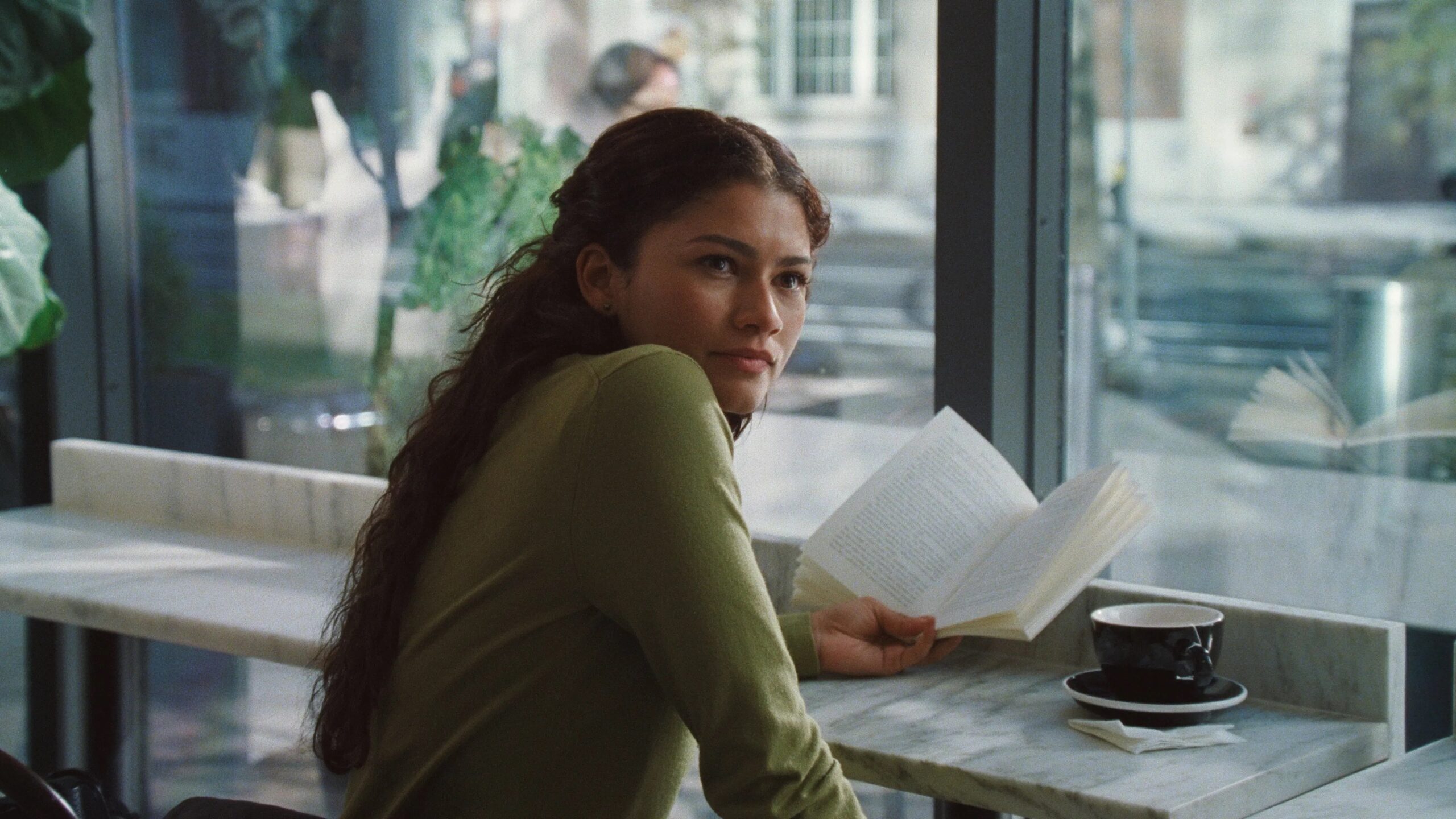 Das Bild zeigt Emma (Zendaya) im Cafè sitzend mit einer Tasse und einem Buch