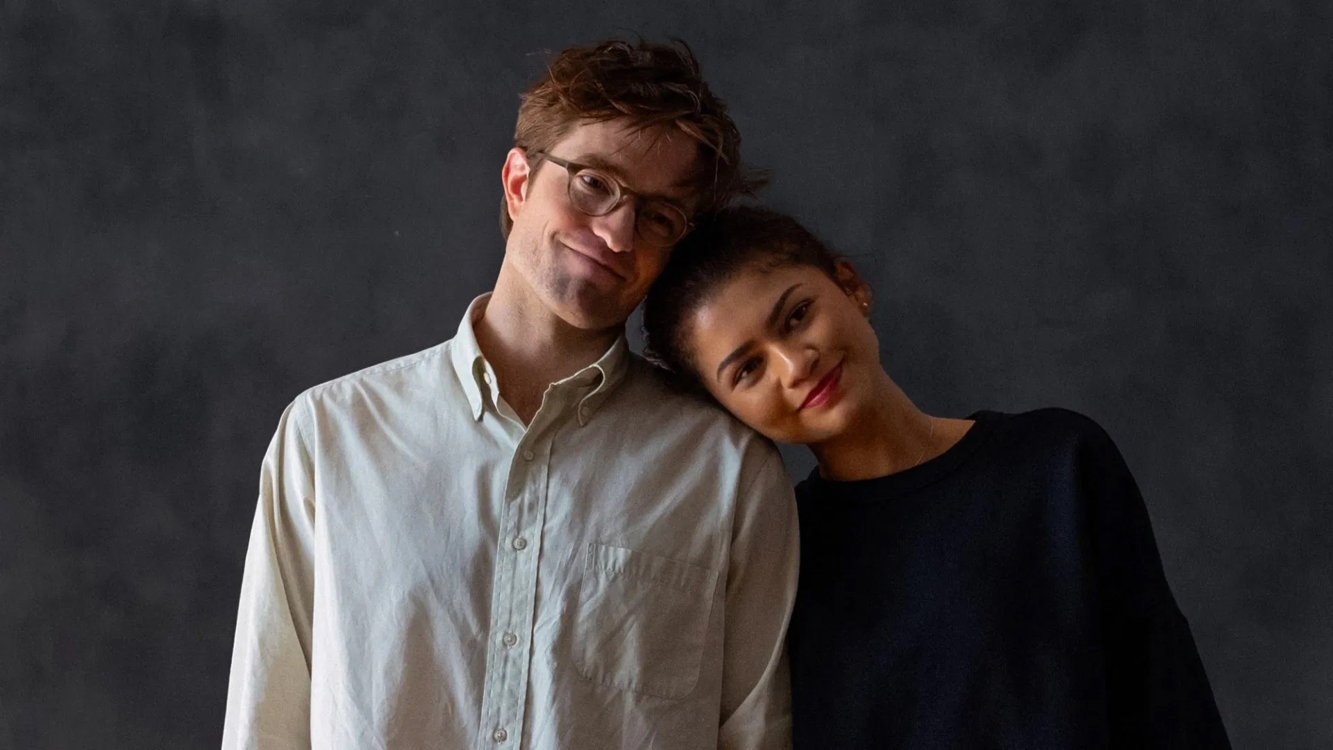 Zendaya lehnt sich an Robert Pattinsons Schulter; eine intime, ruhige Szene vor dunklem Hintergrund.
