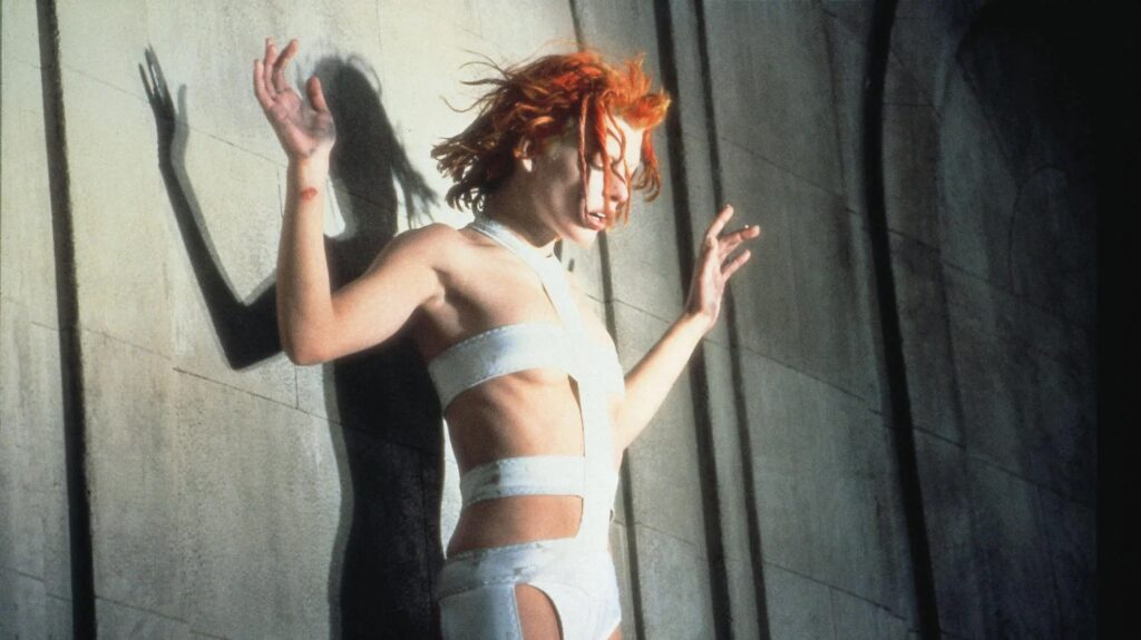 Milla Jovovich als Leeloo aus ‚Das fünfte Element‘ in ihrem ikonischen weißen Band‑Outfit vor einer grauen Wand, futuristische Sci‑Fi‑Ästhetik mit starkem Schattenwurf. | Themenübersicht Mai 2026